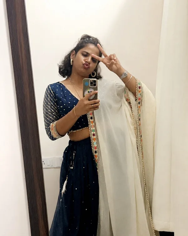 A warm candid portrait, a peace sign, in a navy lehenga and white dupatta.